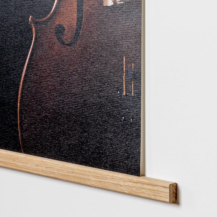 Posterleisten Detail Detailaufnahme einer Posterleiste aus Holz, die ein Plakat hält, mit einem dunklen Hintergrund und einem Teil eines Instruments sichtbar.
