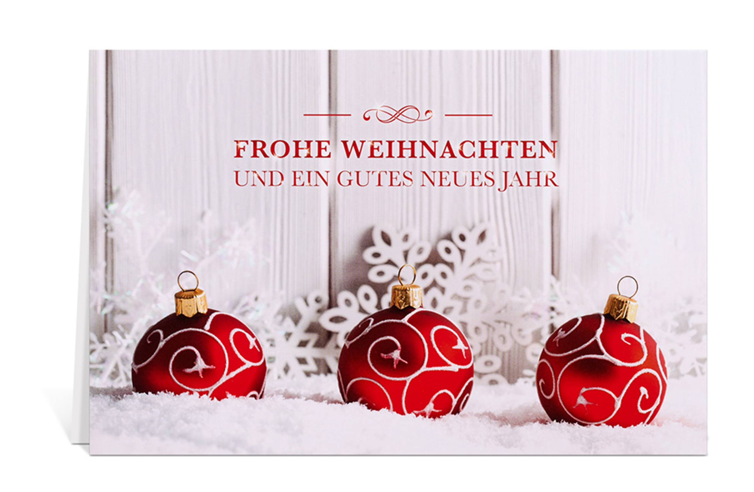 Weihnachtskarte mit drei roten Christbaumkugeln im Schnee vor einer weißen Holzwand, und dem Text: Frohe Weihnachten und ein gutes neues Jahr
