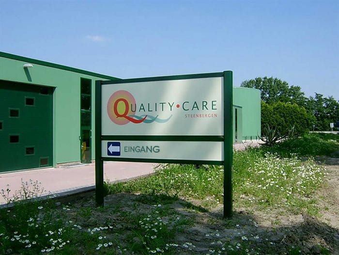 Schild Eingang Lowres Schild mit der Aufschrift 'Quality Care Steinbergen' und dem Hinweis 'Eingang' in Richtung links.