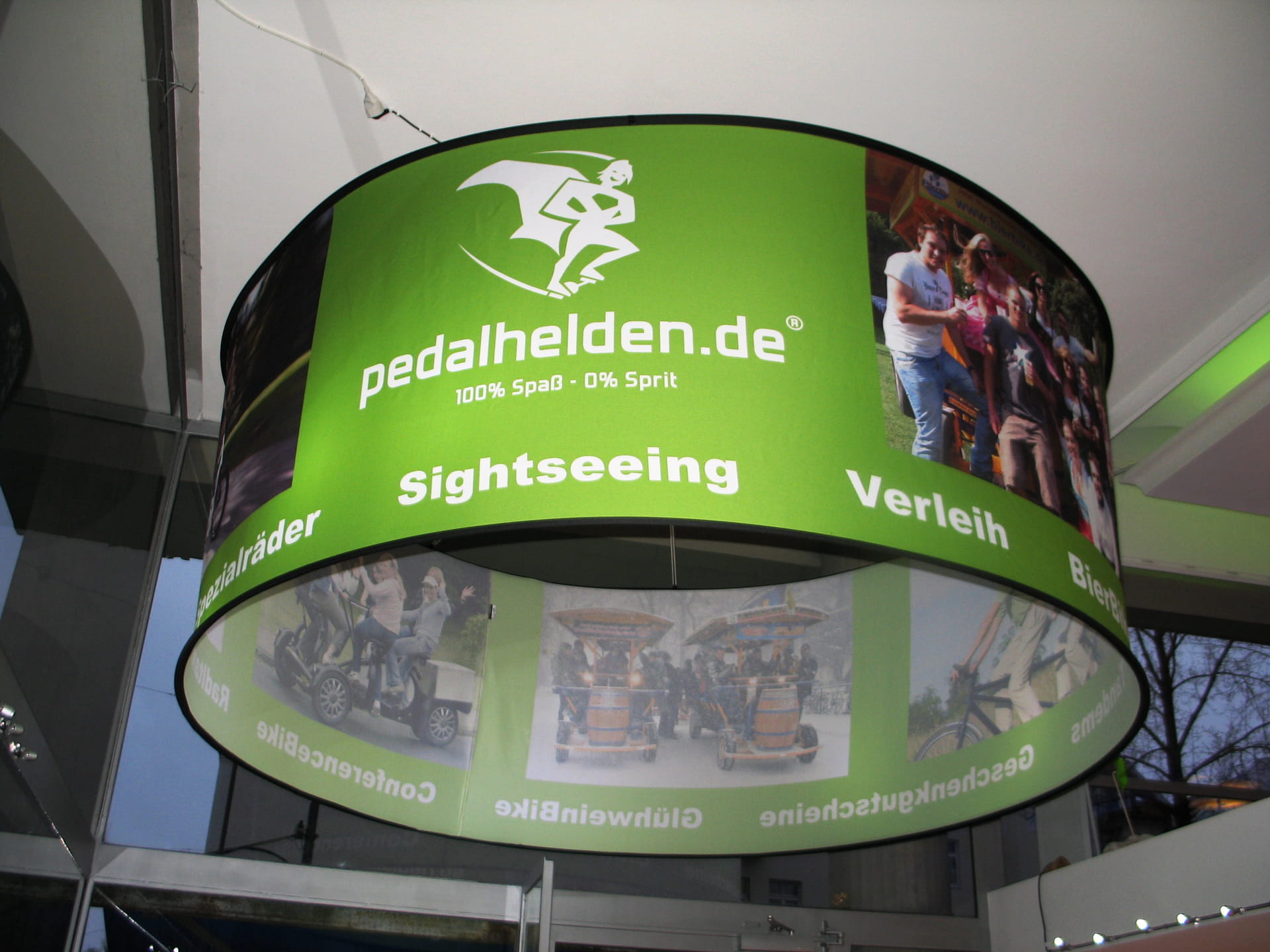 Deckenhänger rund Cylindrical Messe Sparkasse Drei runde Deckenhänger mit dem Schriftzug Hertz hängen über einem Messestand. Im Hintergrund ist der Stand von Europcar sichtbar.
