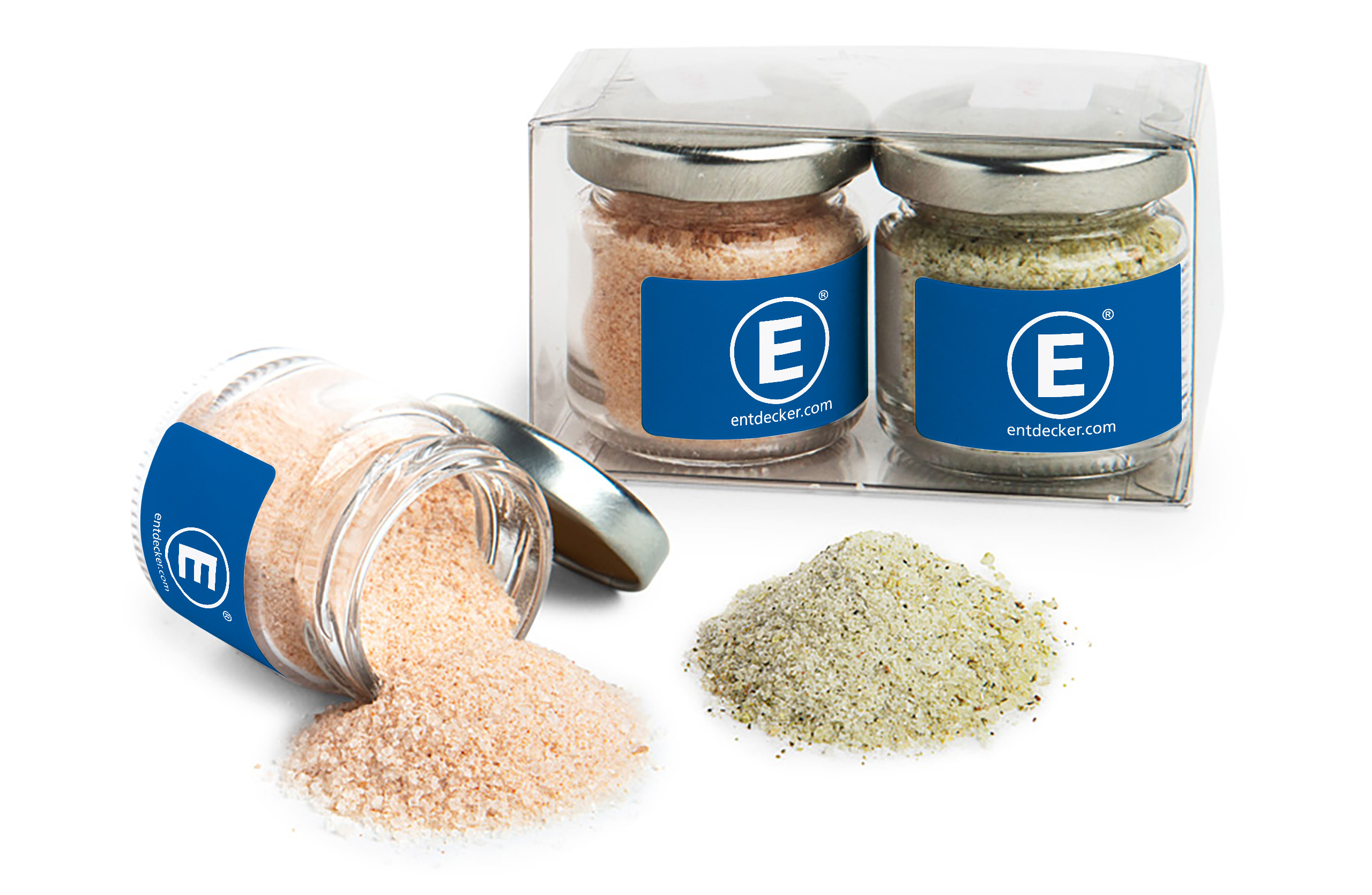 Zwei kleine Salzgläser mit den Gourmetsalz Sorten Dill-Petersilie und Chili-Ingwer in einer transparenten Geschenkbox, daneben ein umgestürztes Glas mit ausgestreutem Salz.