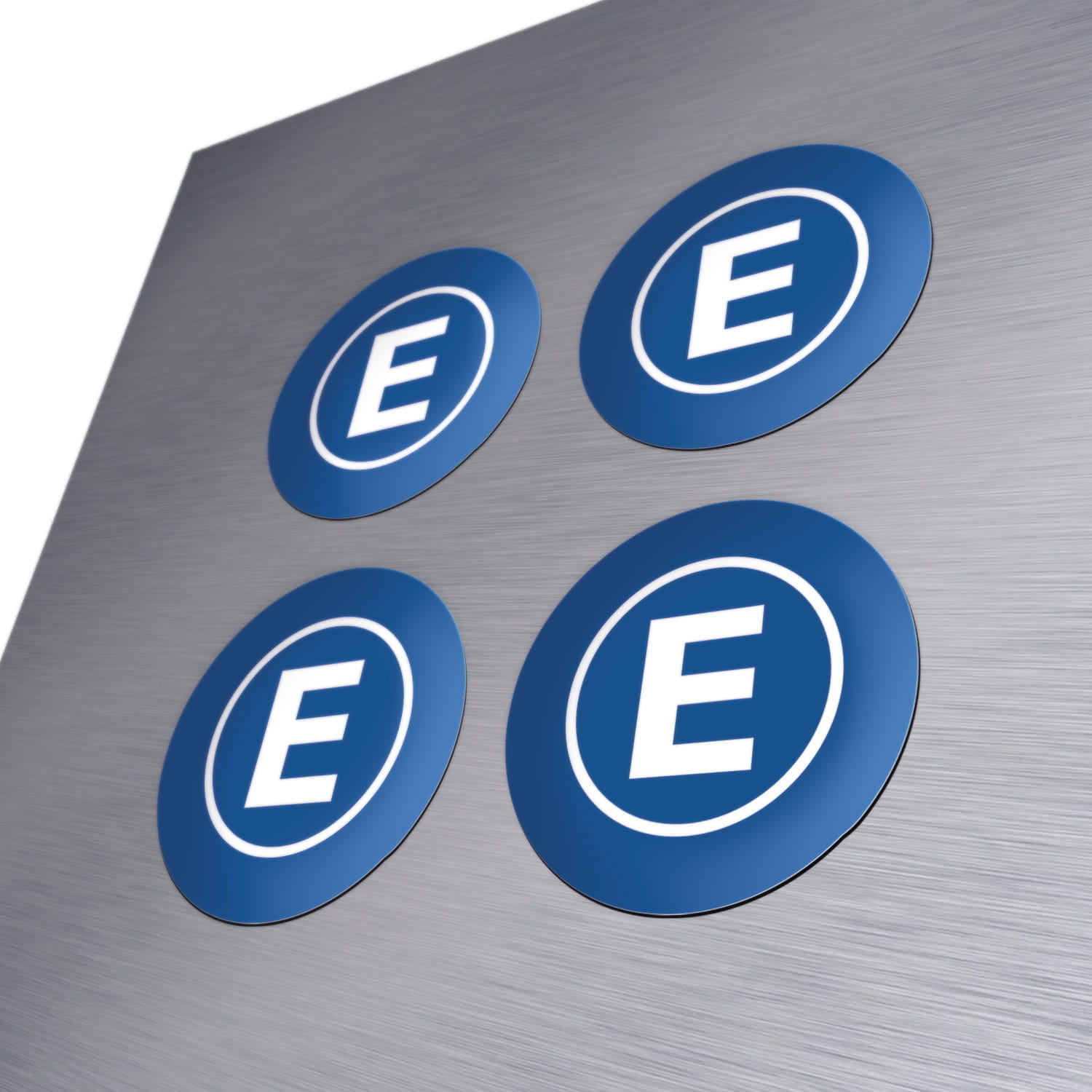 Magnete bedruckt Vier runde, bedruckte Magnete in Blau mit einem weißen E im Kreis, auf einer metallischen Oberfläche.
