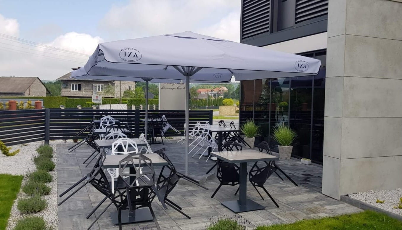 Sonnenschirm Sonnenschirm 13 von ENTDECKER auf einer Terrasse mit Tischen und Stühlen.