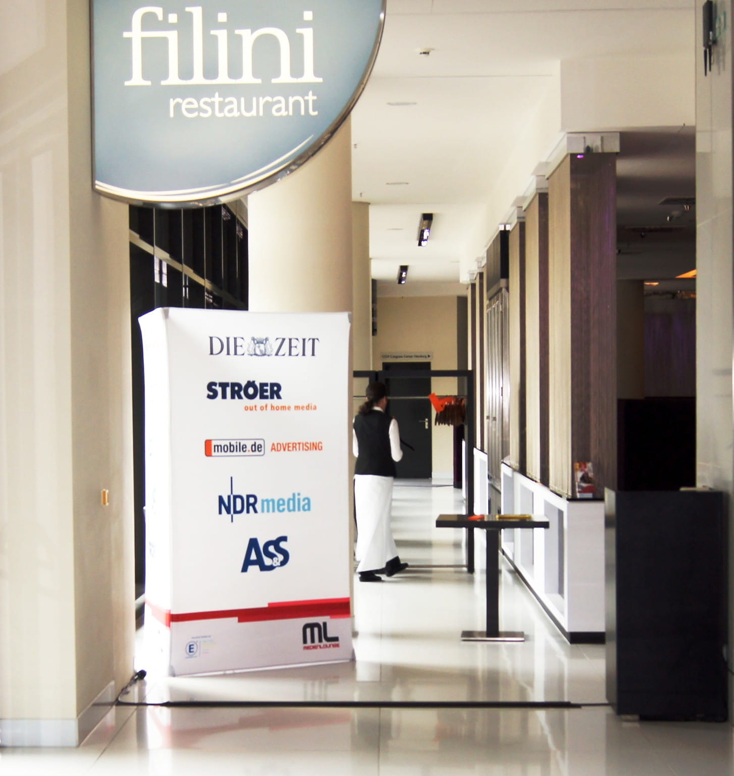 Werbesäule Clickboard Vertical Medienlounge Werbesäule mit Werbung für 'DIE ZEIT', 'mobile.de', 'NDR media' und 'STROER' vor dem Restaurant filini.
