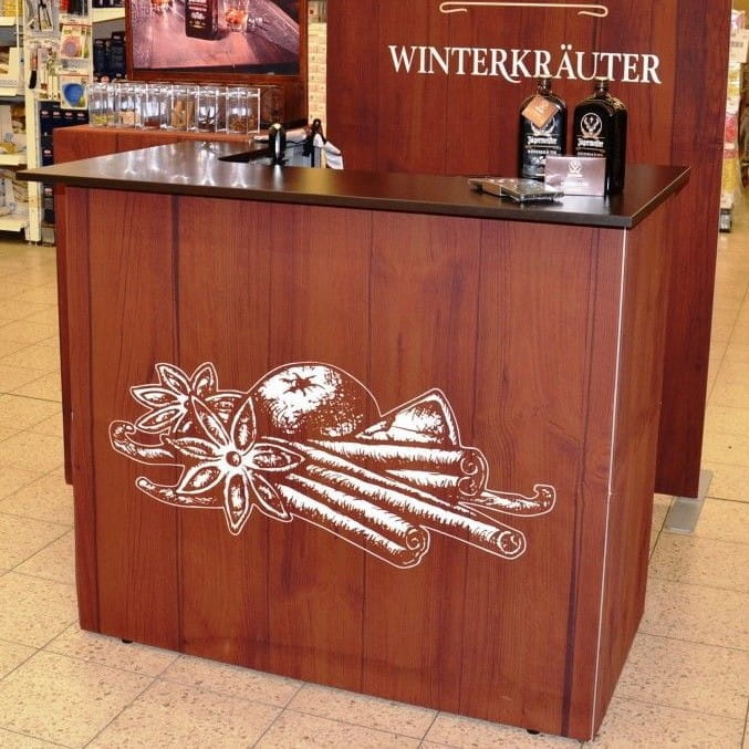 Jägermeister Messetheke Quickup Falttheke Messetheke von Jägermeister mit Holzoptik und schwarzer Arbeitsfläche, dekoriert mit einer Illustration von Gewürzen.