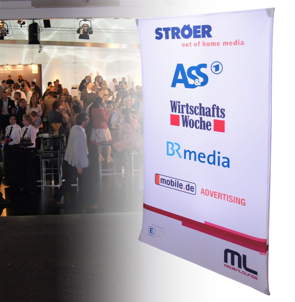 Werbesäule Clickboard Vertical Medienlounge Werbesäule mit Logos von Ströer, ASS, WirtschaftsWoche, BR media und mobile.de, im Hintergrund eine Veranstaltung mit Publikum.