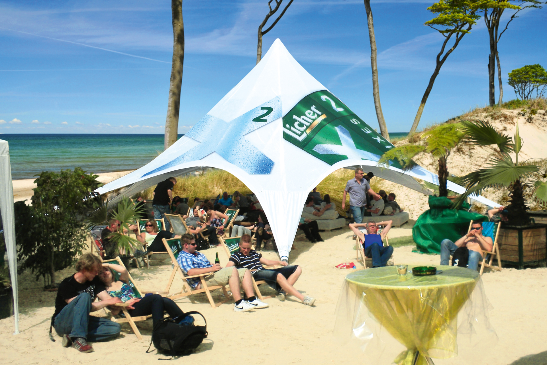 Ein sternenförmiges Zelt am Strand mit Bedruckung von Licher und Liegestühlen