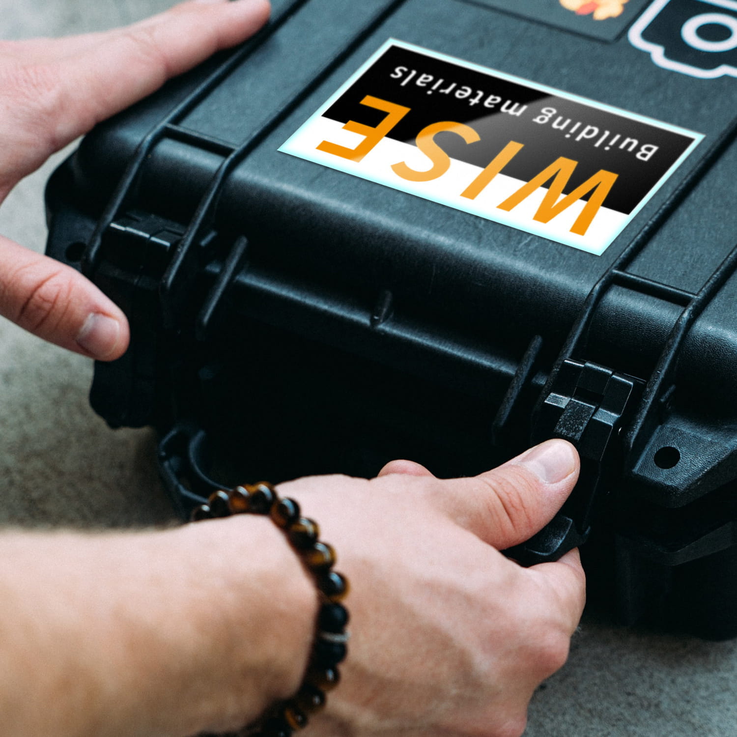 Stoßfeste Folie Koffer Schwarzer Koffer mit stoßfester Folie, der von einer Hand geöffnet wird. Auf dem Koffer steht WISE Building Materials.