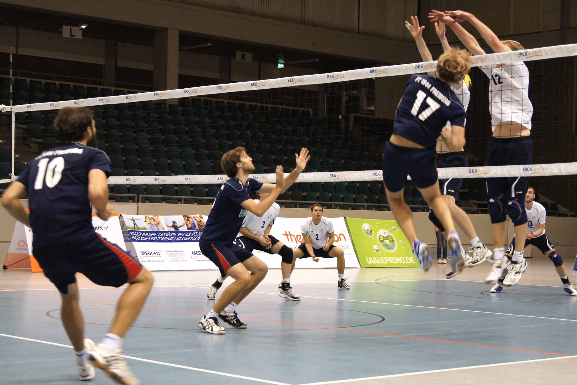 Volleyballspieler in einer Halle springen auf das Netz zu mit dreieckigen Werbeträgern im Hintergrund