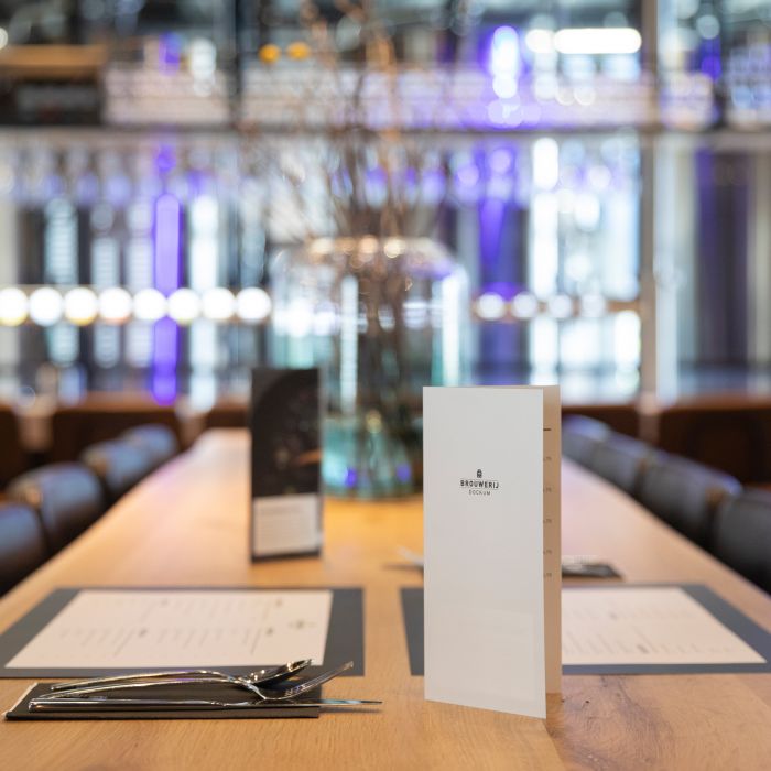 Speisekarten Gastronomie Zwei Speisekarten auf einem Tisch in einem Gastronomiebetrieb, mit Besteck und einem Glas im Hintergrund.