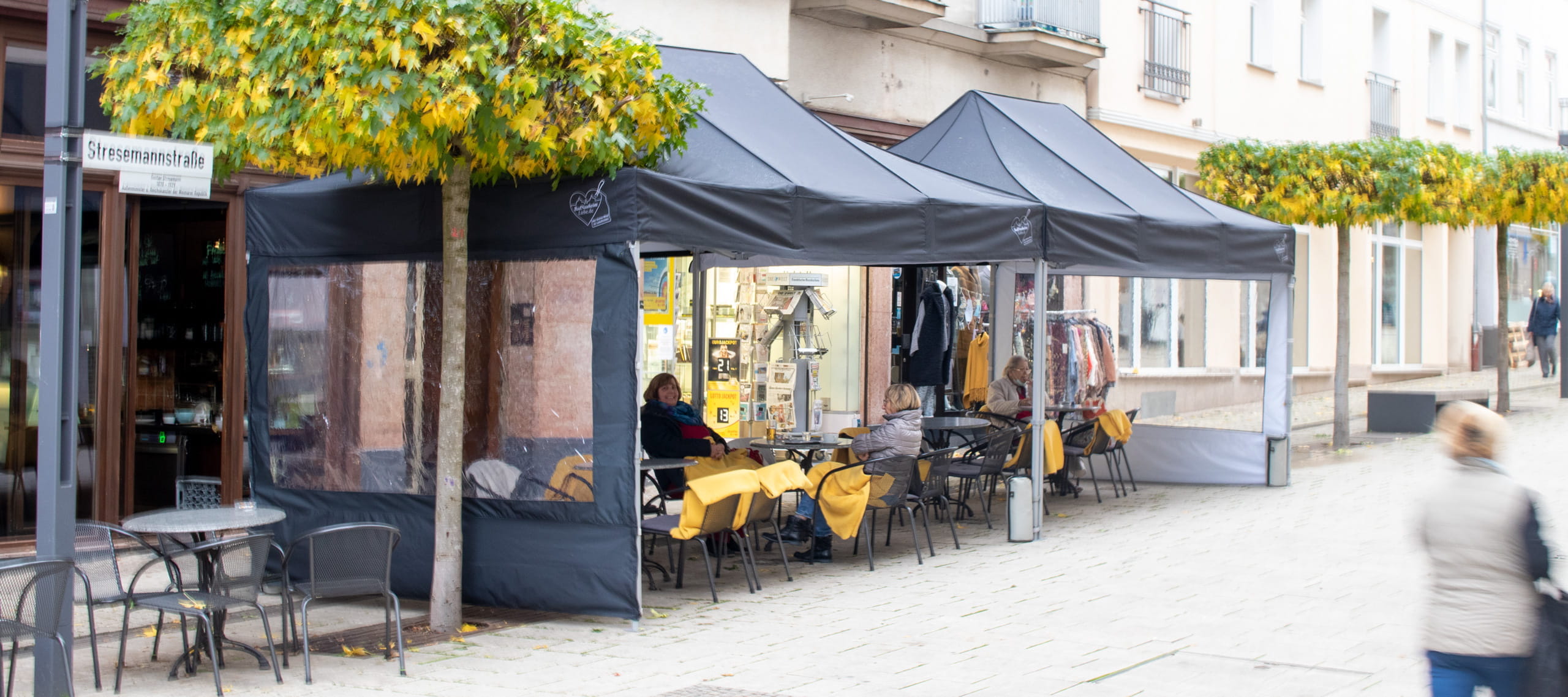 Außengastronomie Zeltaktion Bad Nauheim Zwei schwarze Zelte für die Außengastronomie in Bad Nauheim, mit Tischen und Stühlen, umgeben von Bäumen mit gelben Blättern.