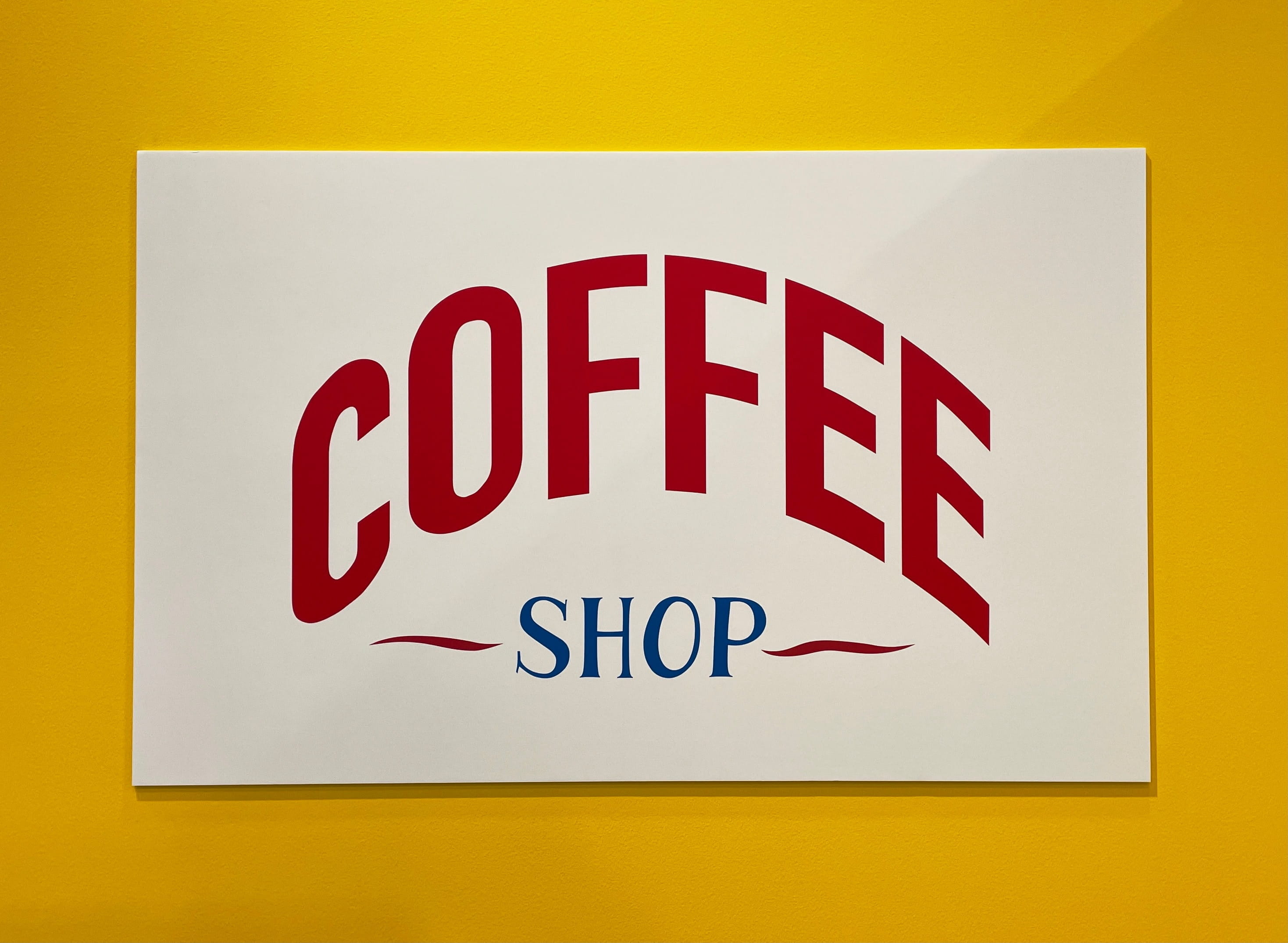 Werbeschild Kaffee Werbeschild mit der Aufschrift 'COFFEE SHOP' in roten und blauen Buchstaben auf gelbem Hintergrund.
