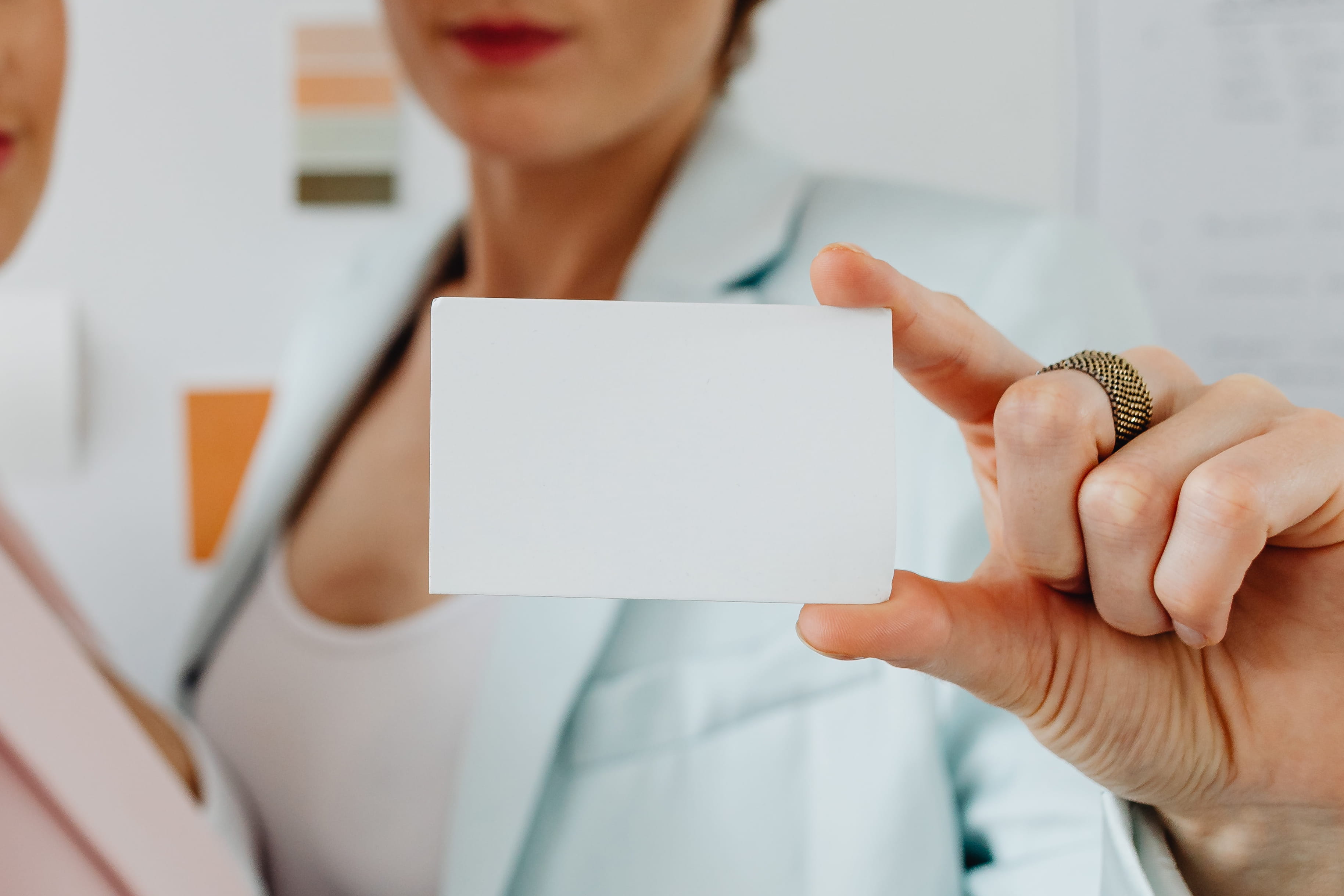 Best Practice mit Ihnen! Zwei Frauen stehen vor einer Wand mit Farbmustern und halten eine leere Karte in der Hand. Eine Frau trägt einen blauen Blazer, die andere einen rosa Blazer.
