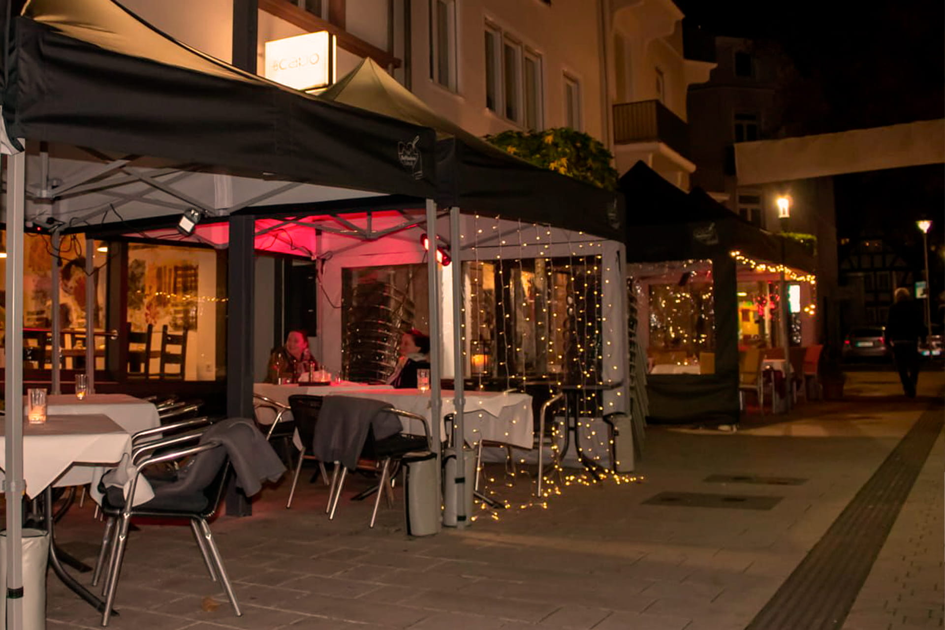 Eine Reihe von Faltzelten in der Innenstadt vor Restraurants mit Tischen und Lichterketten bei Nacht