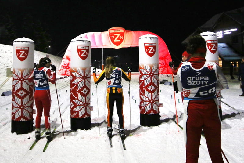 Skilanglauf-Event mit Vento Säule Pzn Blow Up Skilangläufer stehen an der Vento Säule Pzn Blow Up, umgeben von Schnee und beleuchtet von Nachtlichtern.