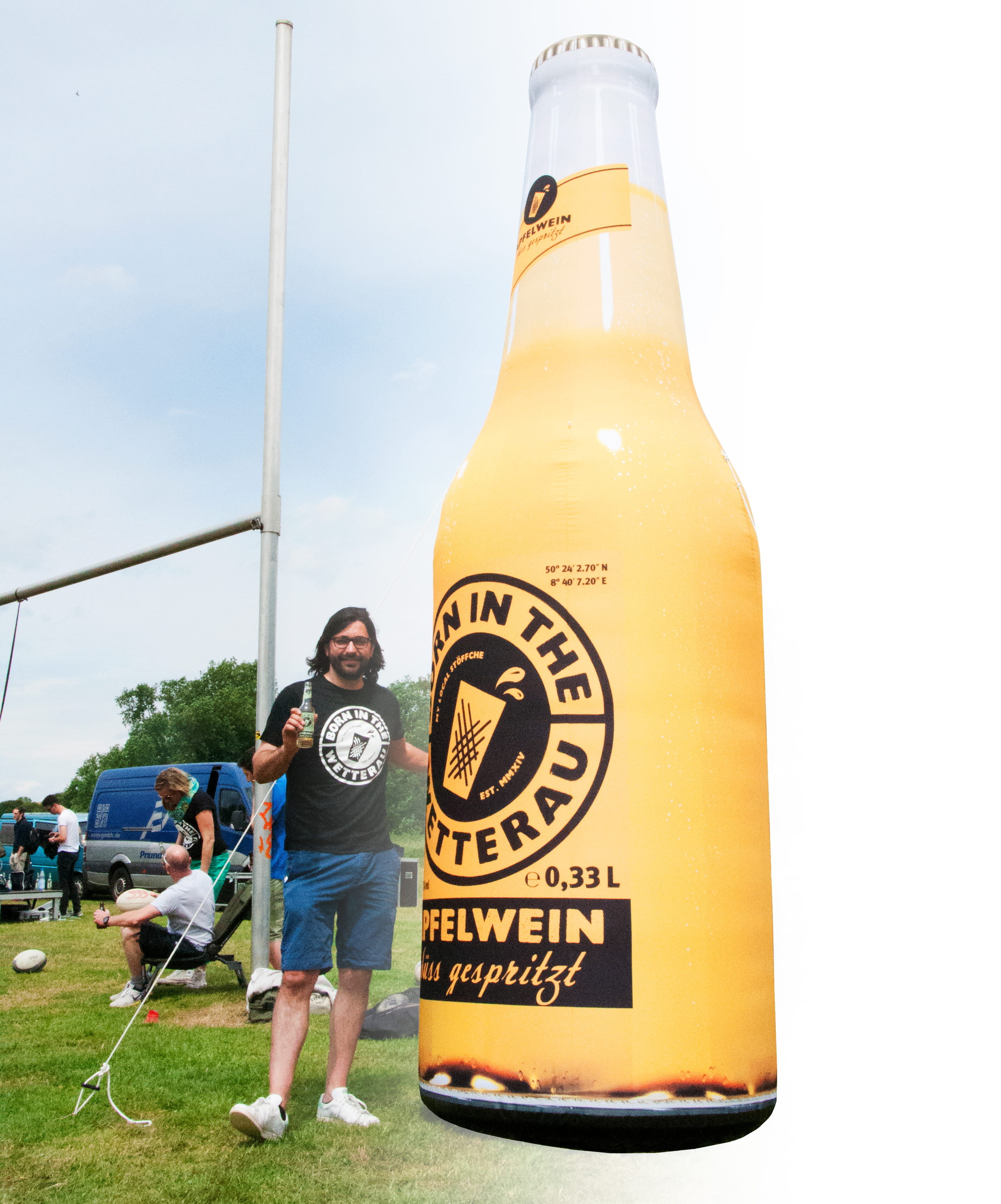 Blow Up Easy Inflate Ad Flasche Born In The Wetterau Mann steht neben einer übergroßen Flasche des Produkts 'Blow Up Easy Inflate Ad Flasche Born In The Wetterau', die Apfelwein bewirbt.