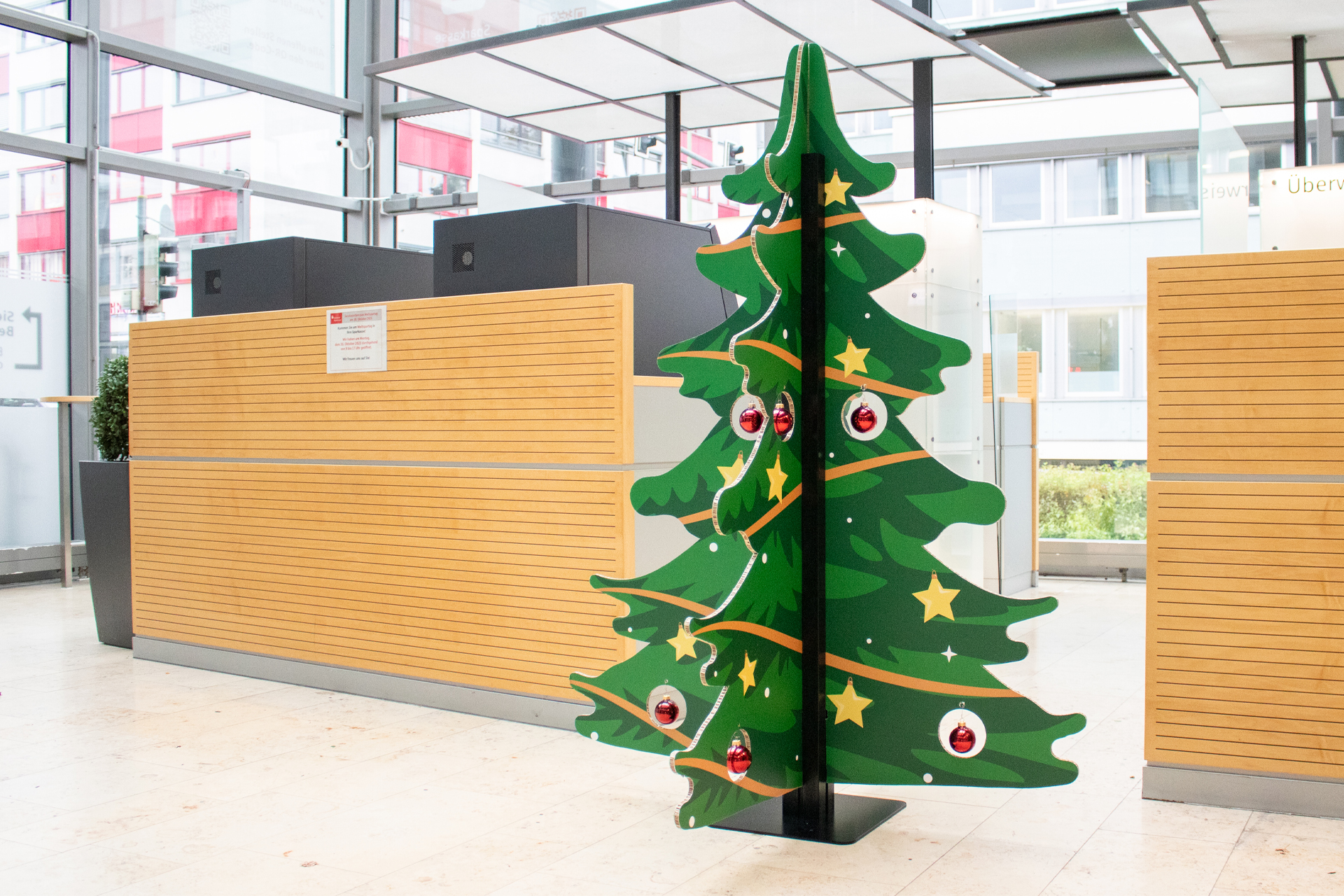 Inhaker Weihnachtsbaum Zusammensteckbarer Weihnachtsbaum aus Wabenkarton mit einhängbaren Weihnachtskugeln in einer Bankfiliale