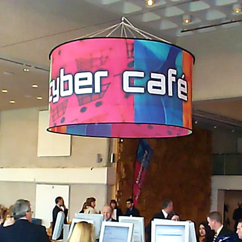 Deckenhänger rund im Internetcafe Runder Deckenhänger mit der Aufschrift 'Cyber Café' im Internetcafé, umgeben von Besuchern und Computerarbeitsplätzen.