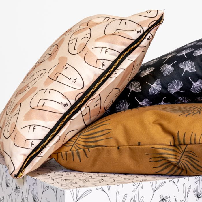 Dekokissen Stapel Dekokissen Stapel in verschiedenen Designs: ein Kissen mit Gesichtern, ein schwarzes Kissen mit floralen Mustern und ein braunes Kissen. Alle haben einen Reißverschluss.
