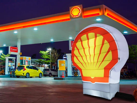 Shell Logo an einer Tankstelle Shell Logo an einer Tankstelle mit beleuchtetem Logo und gelbem Auto im Hintergrund.