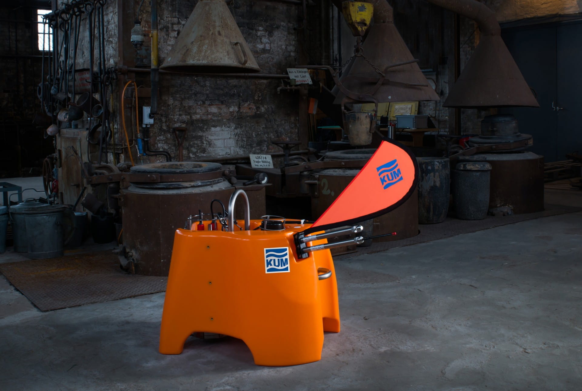 Tischaufstelle Easyflag Micro KUM Tischaufstelle Easyflag Micro von KUM in leuchtendem Orange, mit einem auffälligen roten Flaggenelement, in einer industriellen Umgebung.