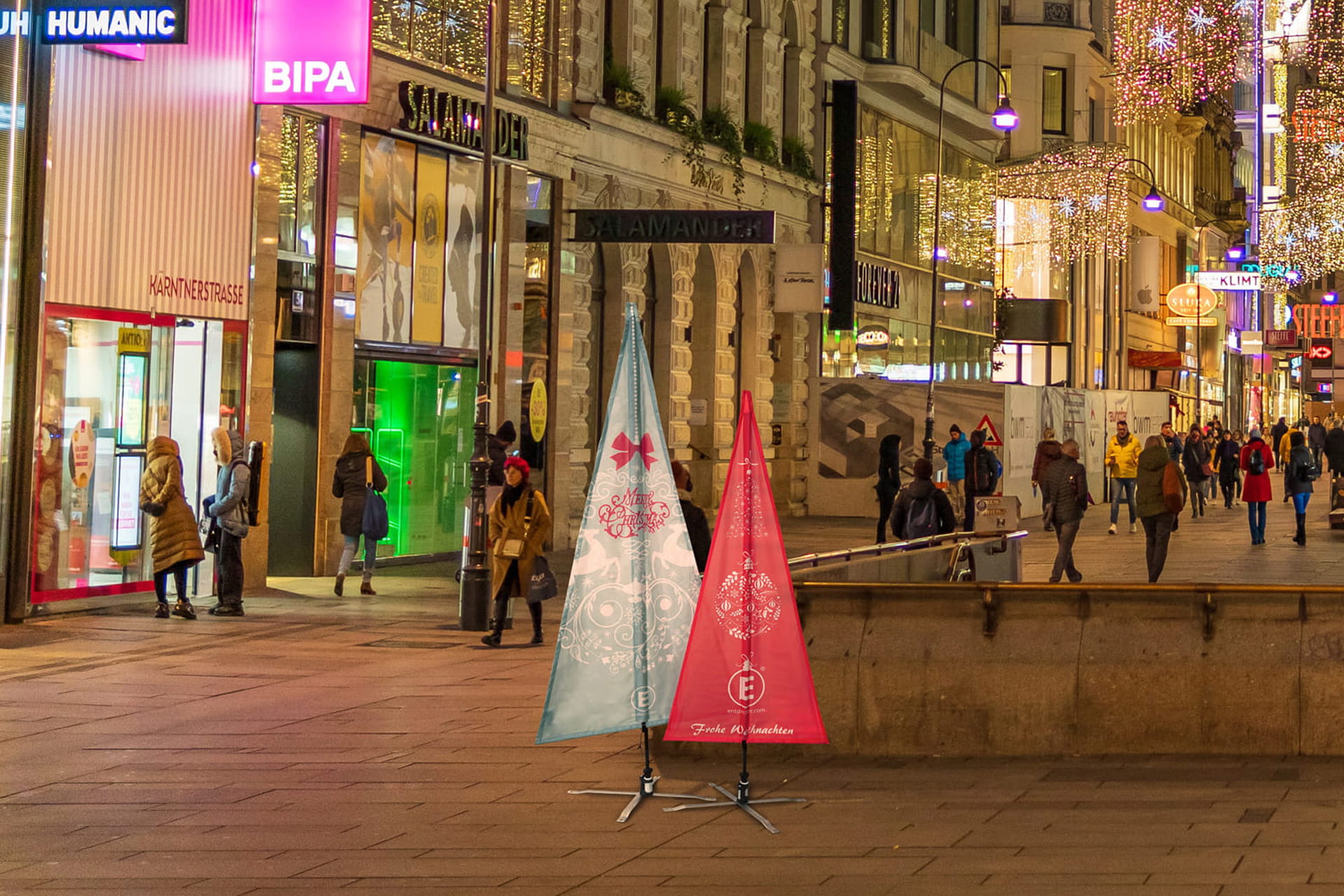 Weihnachtsbaumfahnen Fahnen in Weihnachtsbaumform mit winterlichen Motiven nebeneinander auf einer winterlich geschmückten Einkaufsstraße