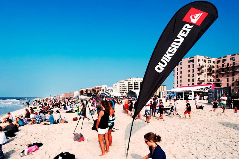 Beachflag Quiksilver am Strand Beachflag von Quiksilver am Strand, umgeben von Menschen und Gebäuden im Hintergrund.