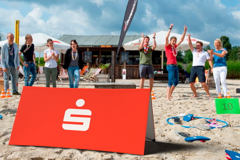 Werbebande Clickboard Strand mit Sparkassen-Logo Werbebande Clickboard Strand mit dem Logo der Sparkasse, umgeben von Menschen, die am Strand feiern.