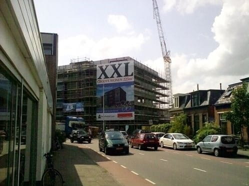 Gerüstbanner Gebäude Gerüstbanner mit der Aufschrift 'XXL' an einem Gebäude im Bau, umgeben von Autos und einer Baustelle.
