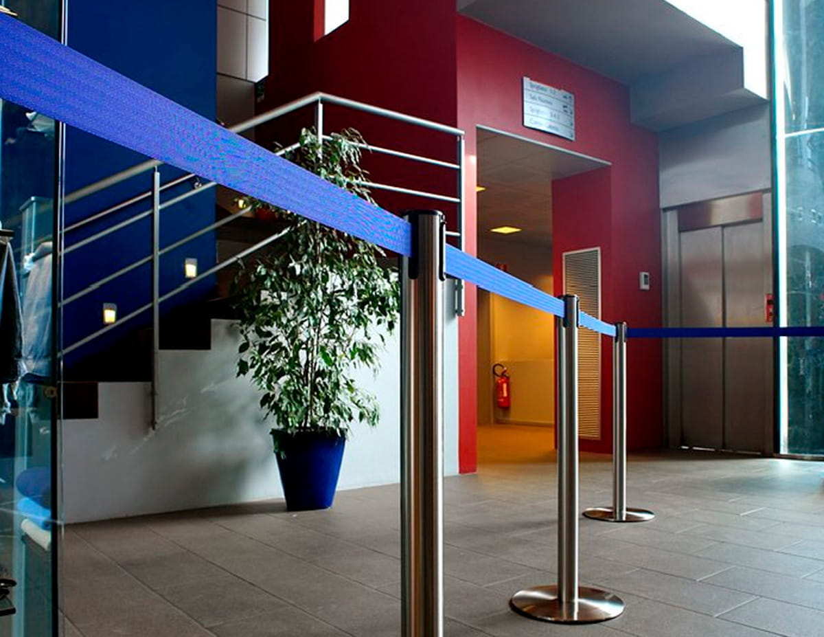 Tensator Einsatzbeispiel Absperrung Tensator Einsatzbeispiel Absperrung mit blauen Absperrbändern und Edelstahlpollern in einem modernen Eingangsbereich.