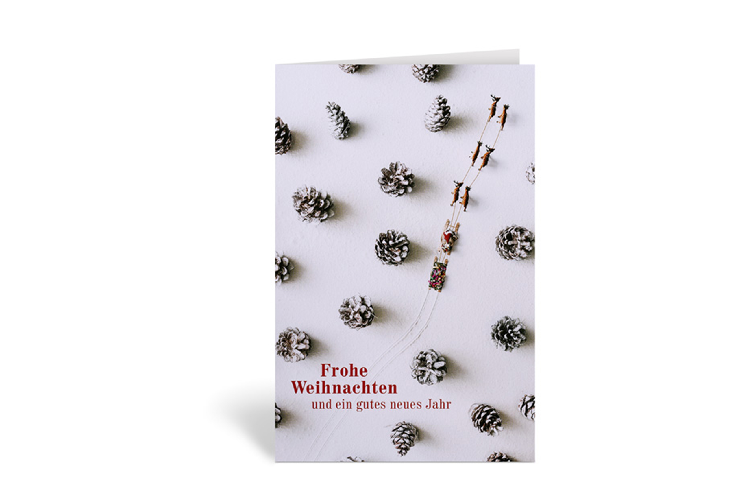 Weihnachtskarte mit einer Vogelperspektive auf einen Wald aus Tannenzapfen, durch den ein Schlitten fährt, zudem der Text: Frohe Weihnachten und ein gutes neues Jahr