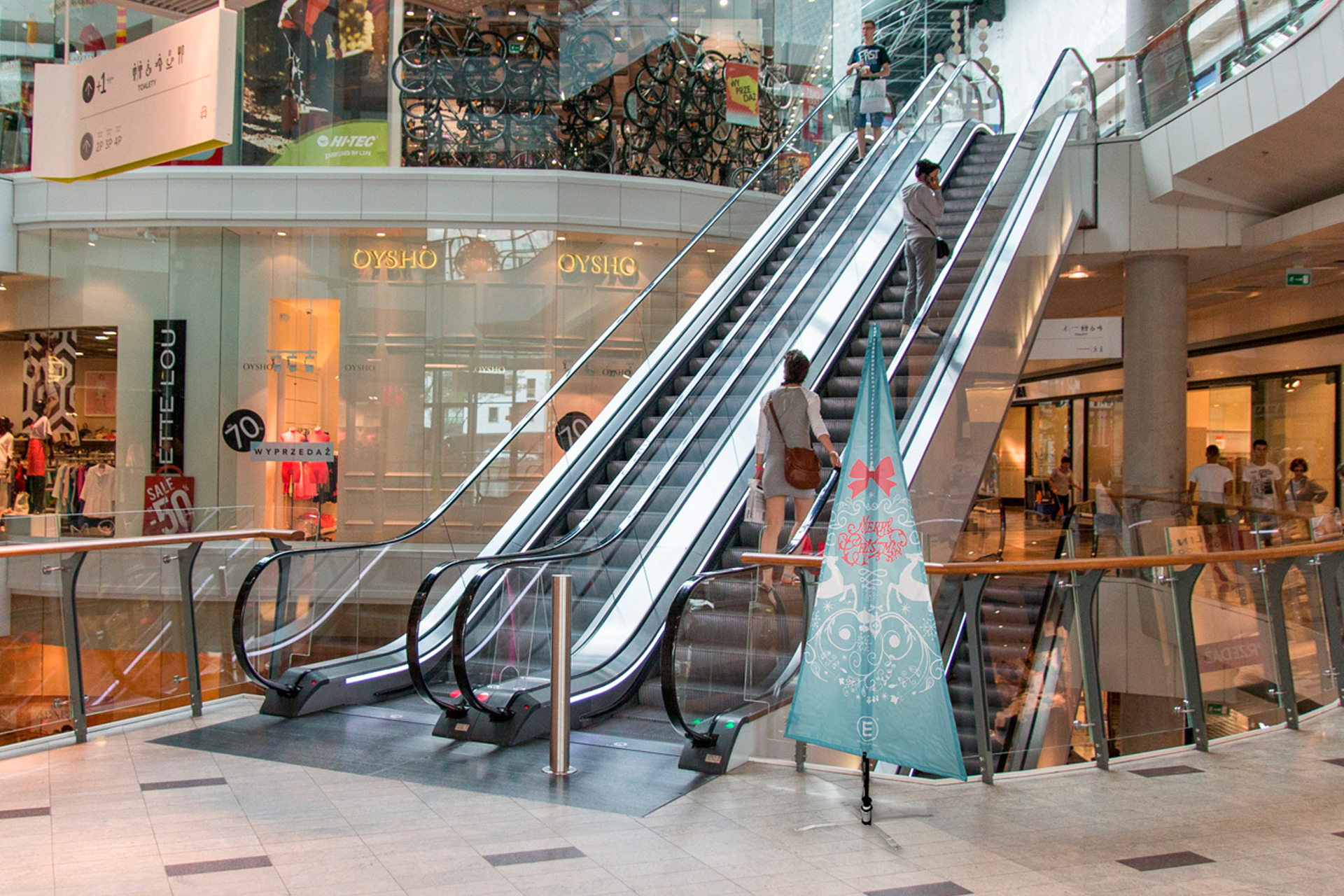 Weihnachtsbaumfahne Fahne in Weihnachtsbaumform mit winterlichem Motiv neben einer Rolltreppe im Einkaufszentrum