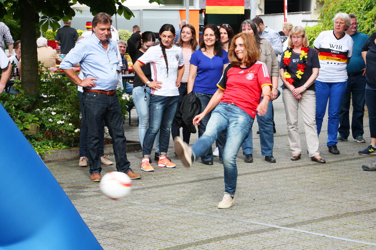 Torwand Fußball Kicker Ein Spieler in einem roten Trikot schießt auf eine Torwand beim Fußball-Kicker-Event. Zuschauer beobachten das Geschehen.
