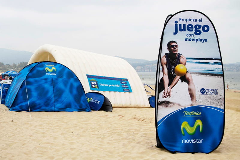 Werbung für Quicktower Strand von Movistar Werbebanner für 'Quicktower Strand' mit einem Mann, der einen Ball am Strand spielt, im Hintergrund ein Zelt und das Meer.