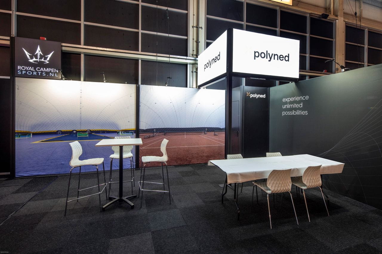 Messestand Inhaker Royalsport Messestand von Royalsport mit dem Produktnamen 'polyned', zeigt Sportplatz im Hintergrund, Tische und Stühle im Vordergrund.