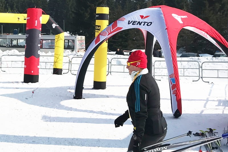 Vento Zelt bei Winterveranstaltung Person in Winterkleidung läuft an einem Vento Zelt vorbei, umgeben von Schnee und Sportequipment.