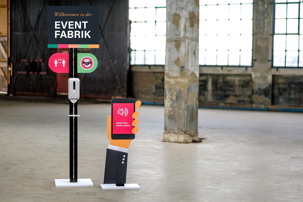 Inhaker Desinfektionsständer Desinfektionsständer mit Handdesinfektionsmittel und Smartphone-Symbol in einer Eventlocation.