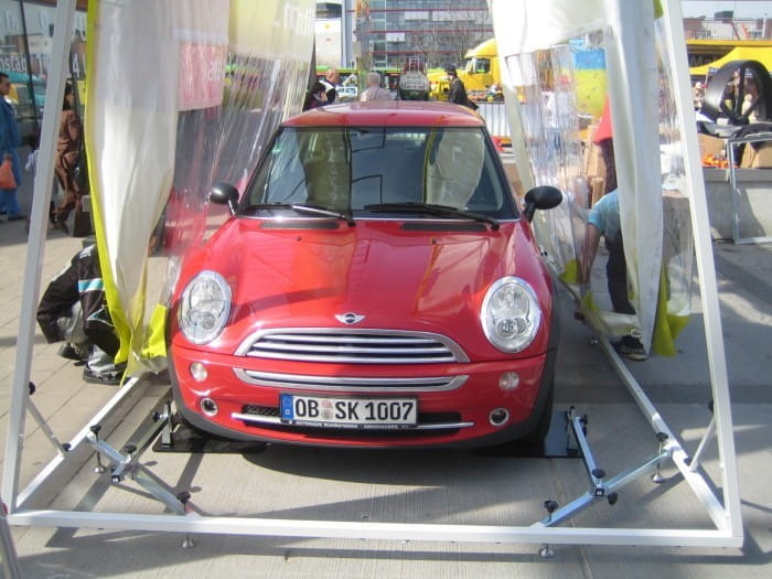 Autotasche Front Aufbau Roter Mini Cooper in einer Autotasche, umgeben von transparenten Wänden, auf einem Veranstaltungsgelände.