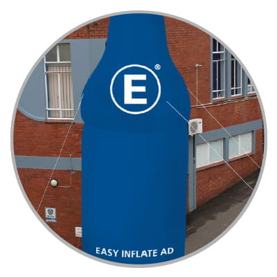 Blow Up Easy Inflate Ad Detail Abspannset Blaues Werbebanner in Flaschenform mit dem Text 'EASY INFLATE AD' und einem großen weißen 'E' darauf, befestigt an einem Gebäude.