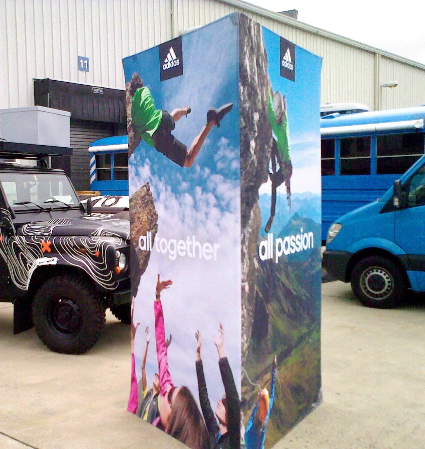 Werbesäule Clickboard Vertical Adidas Werbesäule mit vertikaler Werbung für Adidas, zeigt Menschen beim Klettern und Feiern in der Natur.
