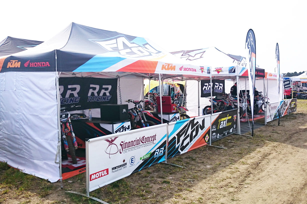 Falcon Faltzelte Easydome Zeltaufbau mit mehreren Faltzelten der Marke Falcon, die für ein Motorsport-Event genutzt werden. Sichtbare Motorräder und Sponsorenlogos.