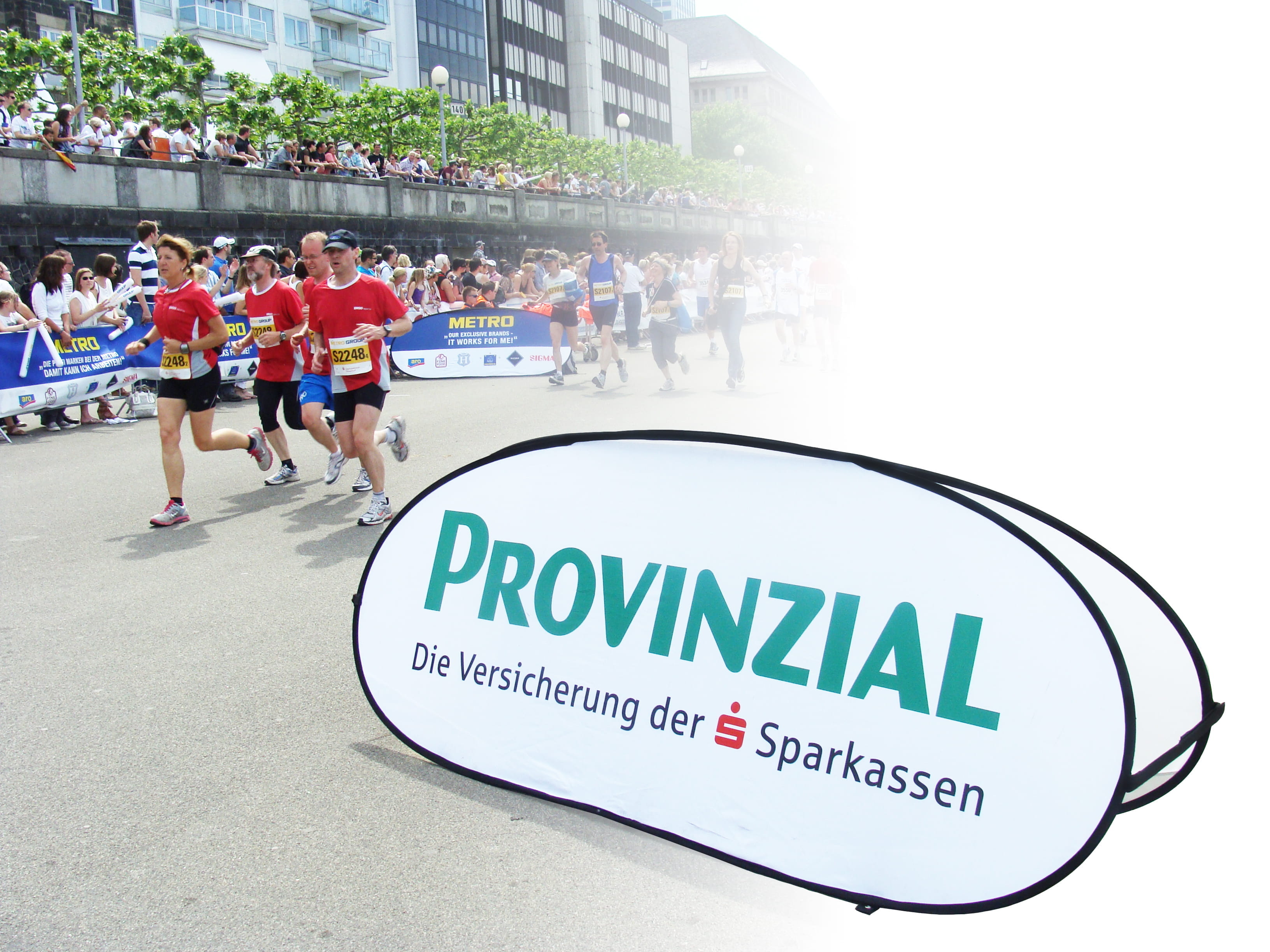 Einsatzbeispiel Quickboard Horizontal Werbebande mit dem Schriftzug 'PROVINZIAL Die Versicherung der Sparkassen' bei einem Lauf-Event, im Hintergrund Läufer und Zuschauer.