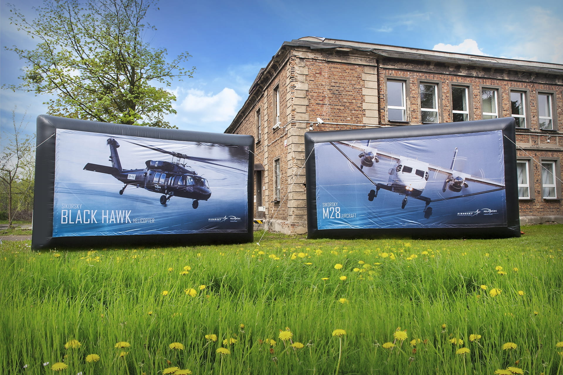 Aufblasbare Wand Vento bedruckt Ein Skifahrer in einem weißen Anzug mit roten und blauen Akzenten fährt an einer aufblasbaren Wand mit dem Aufdruck Vento und Wintersportmotiven vorbei. Im Hintergrund applaudieren Zuschauer.