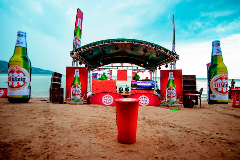Strandbühne für Beach Blow Up Event Bühne am Strand für das Event 'Beach Blow Up' mit großen Bierflaschen-Dekorationen und Lautsprechern.
