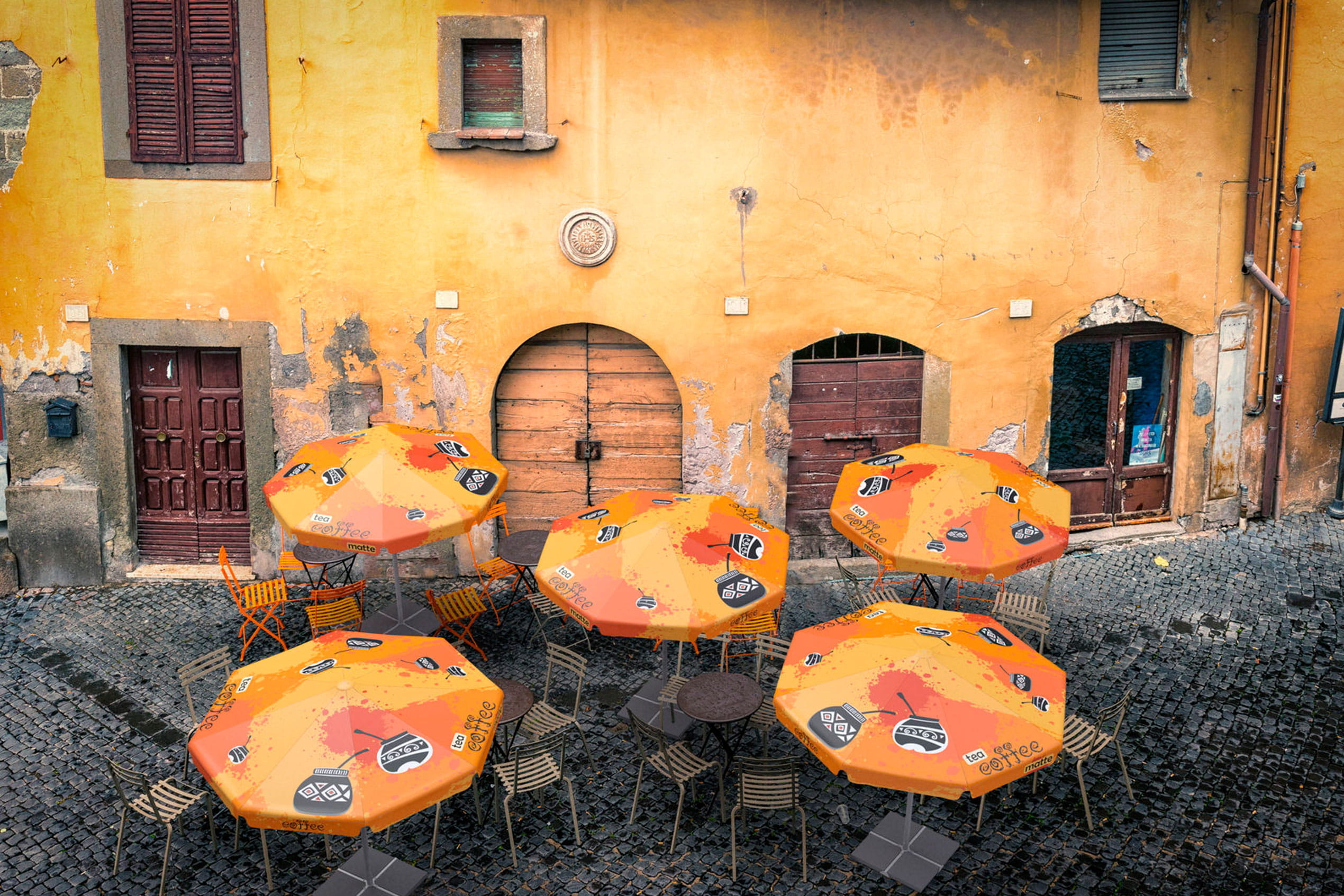 Sonnenschirm Expert Cafe Sonnenschirm Expert Cafe in orange, auf einem gepflasterten Platz vor einer gelben Wand mit alten Fenstern.