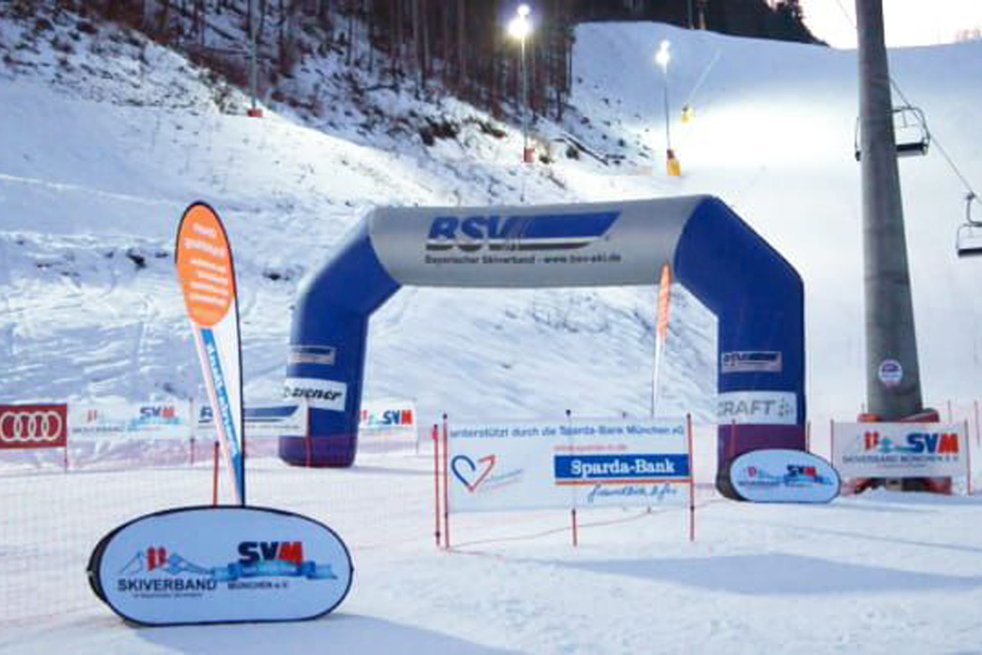 Aufblasbarer Torbogen, Beachflags, Aufsteller und Banner entlang einer Skipiste mit Lift im Hintergrund