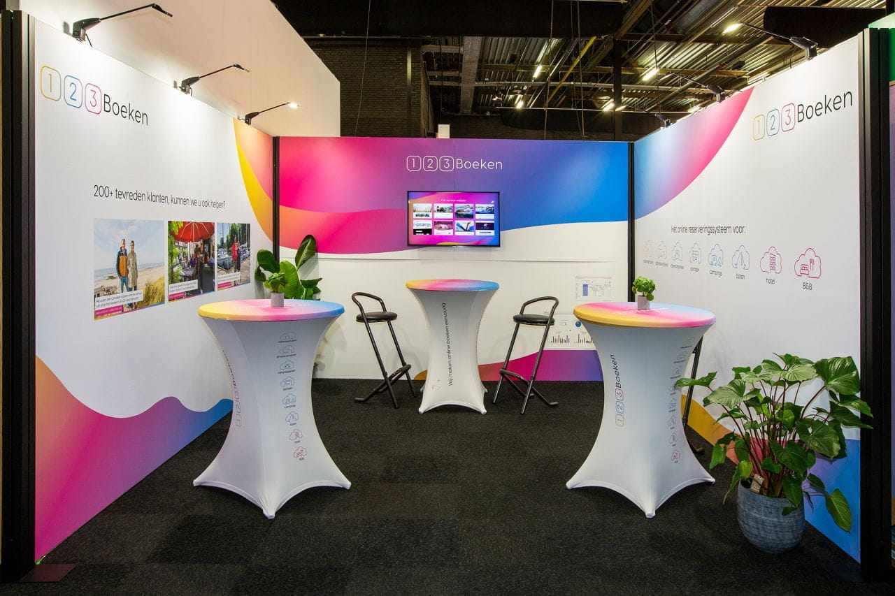 Messestand Inhaker Böken Messestand von 123Boeken mit buntem Hintergrund, Stehtischen und Bildschirm, der Informationen zeigt.