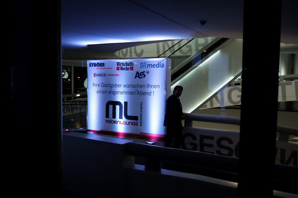 Messewand Quickup Stoffwand Medium Medienlounge Beleuchtete Messewand mit dem Text 'Ihre Gastgeber wünschen Ihnen einen angenehmen Abend!' und dem Logo 'ML Medienlounge München'.