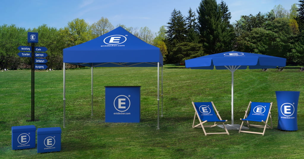 Messe Outdoor Messeoutdoor-Produkt von ENTDECKER: blauer Pavillon, Sonnenschirm, Liegestühle und Werbebanner auf einer Wiese.