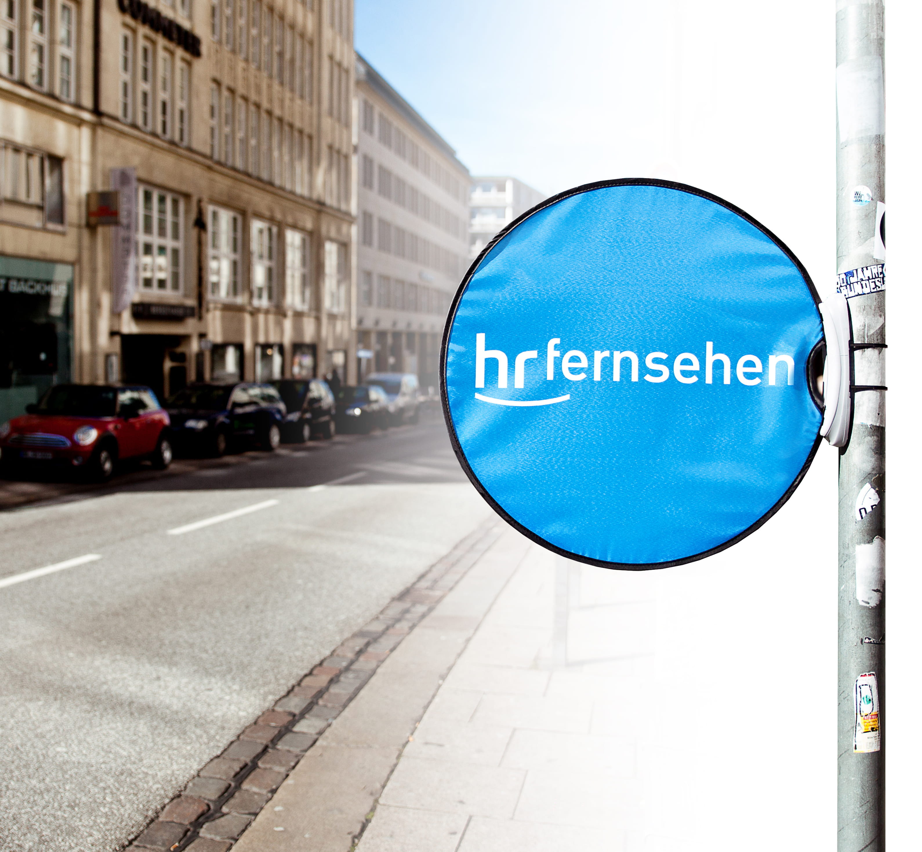 Werbebande Easy Disc Flex HR Fernsehen Werbedisplay Easydisc Flex von ENTDECKER in blauer Farbe mit dem Logo 'hr fernsehen', montiert an einem Straßenpoller.